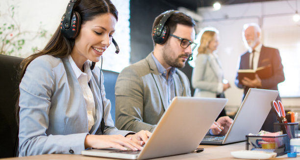 美丽的呼叫中心接线员带着耳机微笑在办公室工作。图片下载