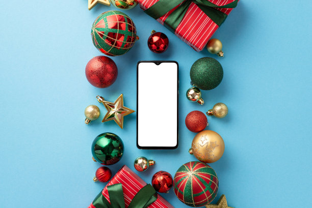 新年概念。俯视图照片的礼品盒彩带蝴蝶结智能手机红色绿色金色装饰物球和星星点缀在孤立的浅蓝色背景与空白图片下载