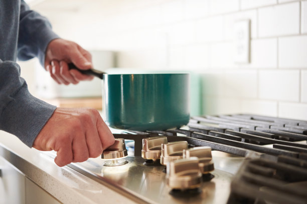 一名身份不明的中年男子站在明亮的现代白色厨房的煤气炉旁图片下载