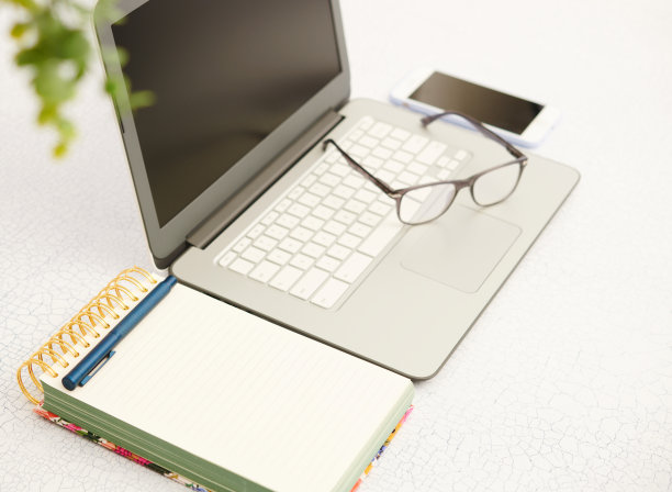 商务静物与笔记本电脑在明亮的办公室设置。键盘上的眼镜和悬挂的植物图片下载