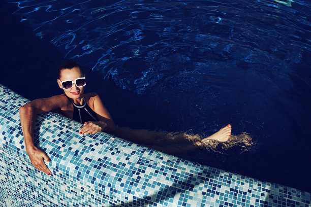 一个穿着黑色泳装和白色太阳镜的女人在游泳池游泳的复古照片图片下载