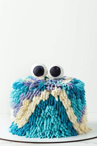 白色背景上可爱的怪物蛋糕。有趣的生日蛋糕与绿松石和蓝色蓬松奶油奶酪糖霜装饰乳脂可食用的眼睛在顶部。幽灵般的孩子万圣节派对蛋糕图片下载