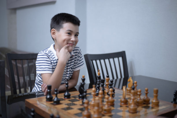 在象棋课上，穿着白t恤的帅气可爱的男孩和他的对手下棋。教育理念，智力游戏。图片下载