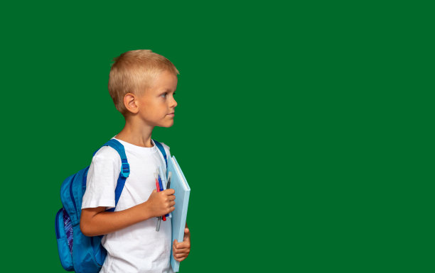 男孩背着背包，手里拿着书和马克笔，看向别处。绿色背景与文本空间。有选择性的重点。关于孩子，学校，教育的文章图片。图片下载