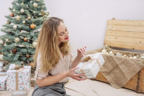 时尚、现代的千禧一代女性坐在人造圣诞树前，手里拿着礼物，面带微笑图片下载