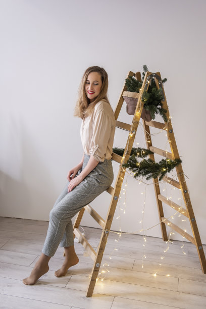 现代中年妇女的肖像在木梯，冷杉树枝，圣诞花环图片下载
