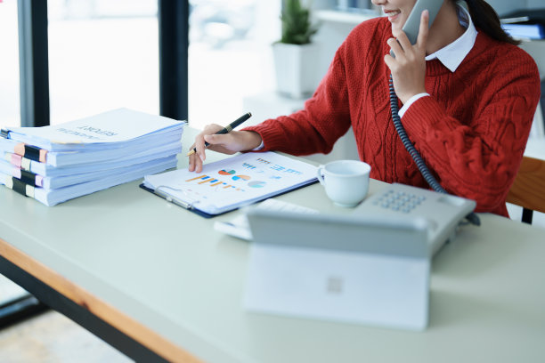 这是一名年轻的亚洲女性的照片，她在凌晨使用她的手机、电脑和桌上的财务文件时露出了微笑图片下载