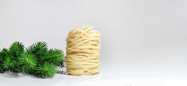 圣诞意大利面。意大利细面条，以塔的形式，孤立在白色背景上，有坚硬的阴影和反射，旁边是圣诞树。巢状的意大利面。意大利面的创意照片。图片下载