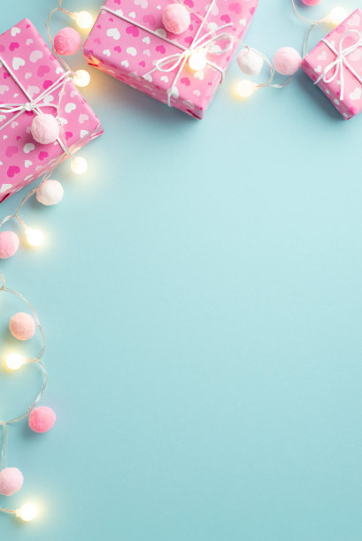 情人节的概念。顶部查看礼盒在包装纸与心形灯泡花环和蓬松的绒球孤立粉彩蓝色背景与文案空间垂直照片图片下载