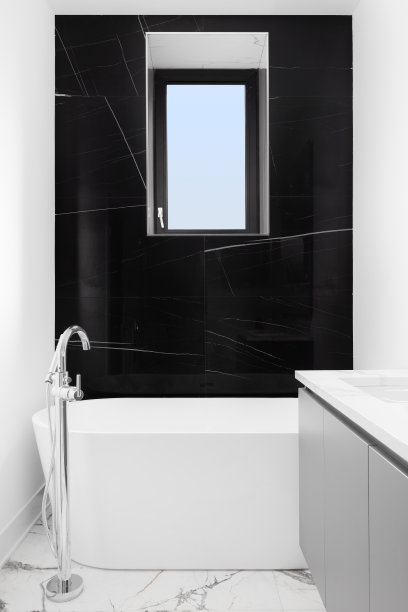 一个独立的浴缸，前面的黑色大理石强调墙。图片下载