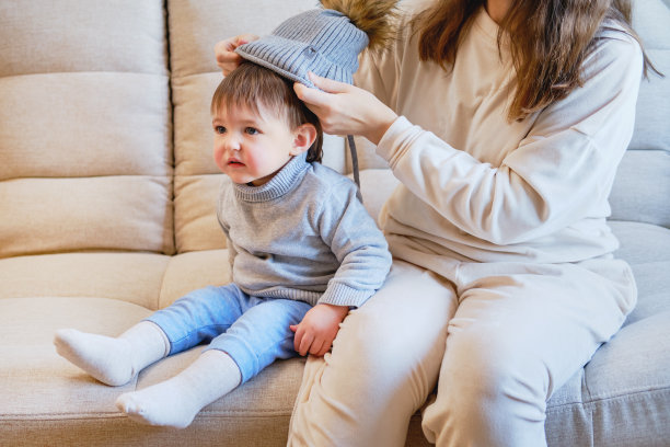 孩子正穿着暖和的冬装在外面散步。寒冷的天气里，母亲给蹒跚学步的男婴穿上衣服。一岁五个月大的孩子在家里的客厅里图片下载