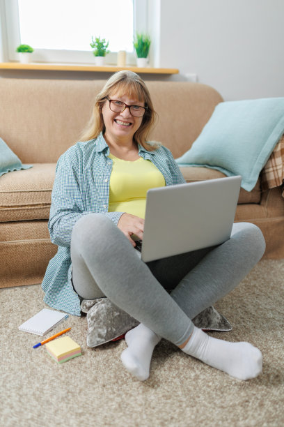 快乐的金发女商人笔记本电脑看着你坐在客厅的地板上，在网上冲浪图片下载
