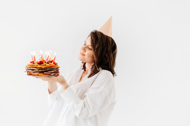 一个快乐的女人拿着一个插着蜡烛的生日蛋糕。图片下载