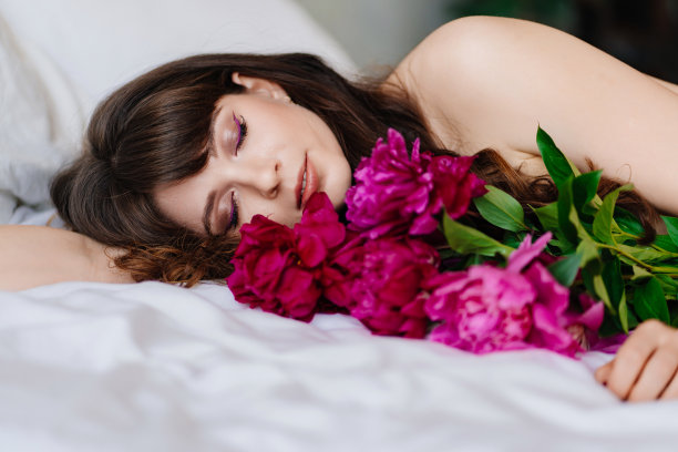 一个迷人而性感的年轻女子捧着一束牡丹躺在床上。图片下载