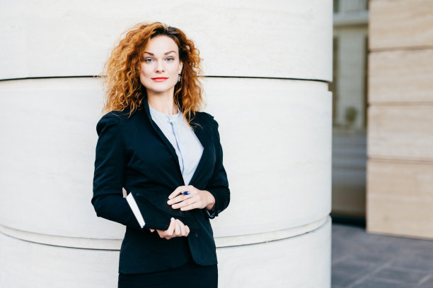 女商人，一头鬈曲的浅色头发，涂着红唇，穿着白色衬衫，黑色夹克和裙子，拿着笔记本和笔，准备写下必要的笔记。人，成功，经营理念图片下载