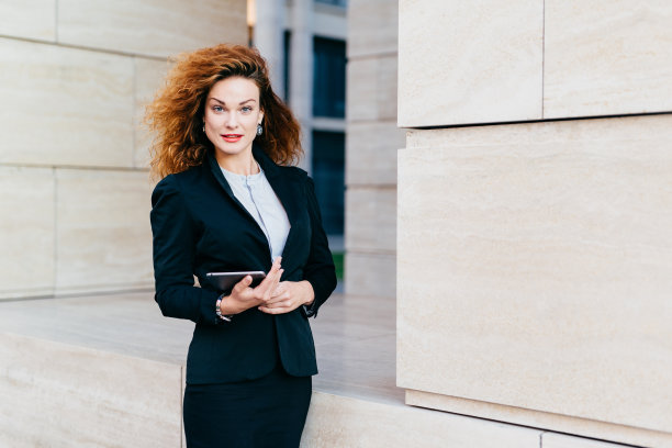 年轻成功的女商人，穿着优雅的衣服，有着华丽的头发，手里拿着平板电脑上班。华丽的女性手持数字平板电脑。科技与商业图片下载