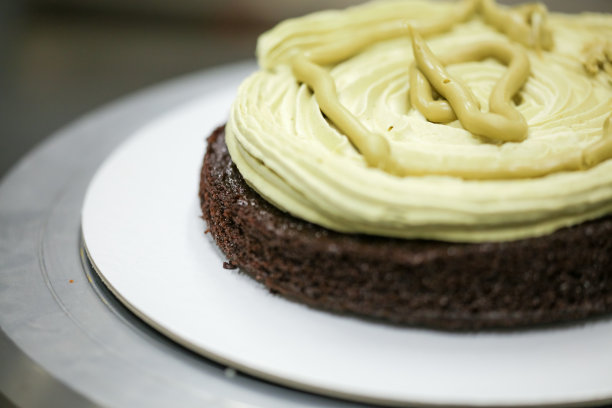 蛋糕厨师设计师使用开心果奶油和洒在分层的黑磨砂巧克力蛋糕在厨房实验室图片下载