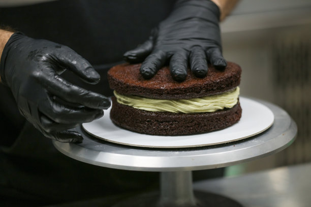 蛋糕厨师设计师使用开心果奶油和洒在分层的黑磨砂巧克力蛋糕在厨房实验室图片下载