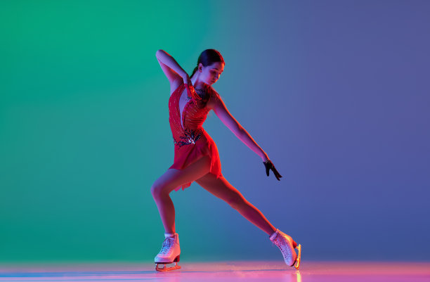 冬季运动。一位身着红色舞台服装的年轻女子花样滑冰运动员展示了基本的花样滑冰元素，在霓虹灯的蓝绿色背景下，动作被隔离开来。图片下载