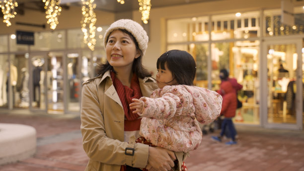 在灯火辉煌的城市街道上，快乐的亚洲妈妈举起手，看着雪花在空中飞舞，孩子抱在怀里好奇地指指点点图片下载