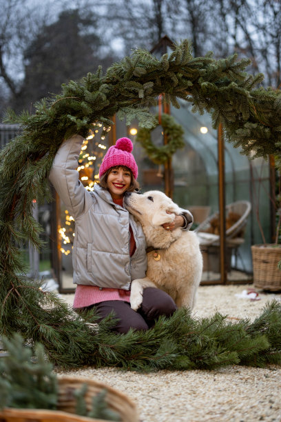 在后院，一名妇女带着一只在圣诞花环中的狗图片下载