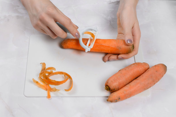 女性用蔬菜削皮器清洗胡萝卜。清洗蔬菜图片下载
