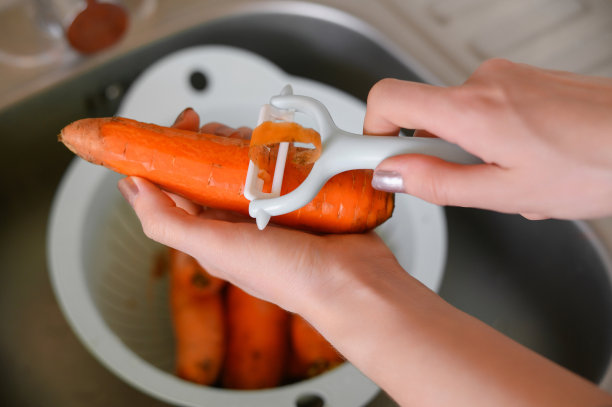 女性用蔬菜削皮器清洗胡萝卜。清洗蔬菜图片下载