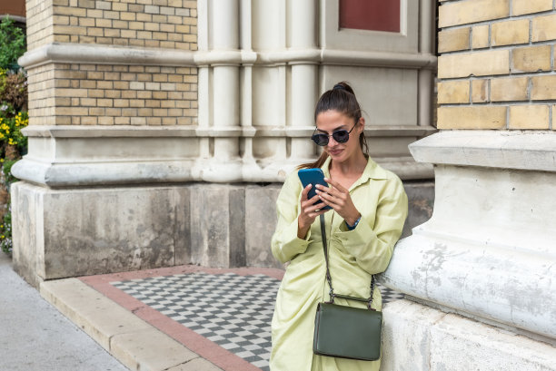 年轻时尚性感的时尚模特女人在美丽的绿色连衣裙温暖的春夏天气户外。时尚风格极客漂亮迷人的女孩在街上与智能手机。图片下载