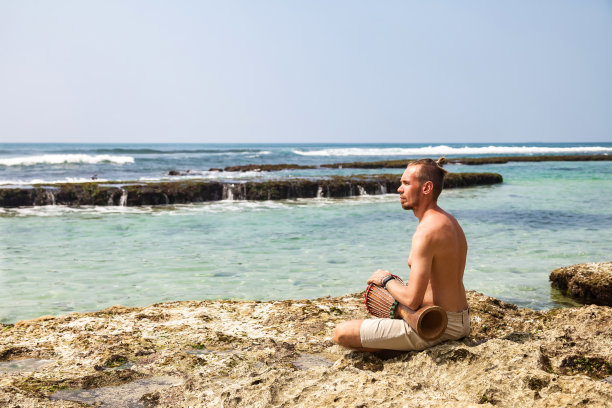 大胡子青年鼓手，演奏节奏与鼓，坐在热带珊瑚礁海岸在海洋背景。旅游度假和音乐放松的概念。有选择性的重点。复制文本空格图片下载