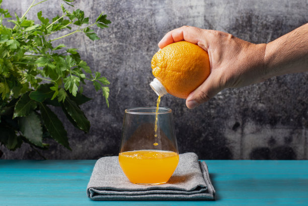 手拿着一个水果，橙子，它有一个喷嘴，它把果汁倒进玻璃杯，就像一个瓶子，特写。图片下载