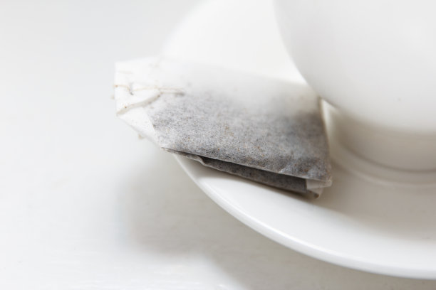 茶托上放着一个纸茶包，旁边放着一杯煮香茶的开水图片下载