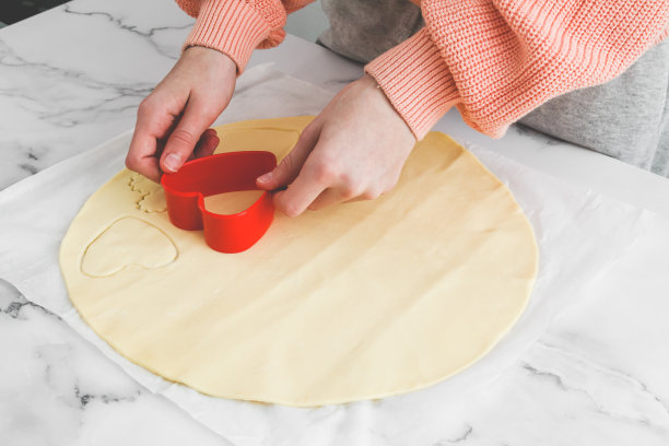 白人少女用红色塑料心形模具切割黄油酥饼图片下载