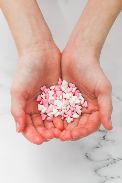 一个白人孩子的手从他们的手掌中拿着粉红色和白色的心。图片下载