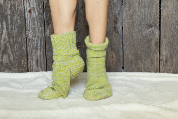 冬天，在家里的房间里，女性的腿穿着绿色的袜子，在白色的地毯上图片下载