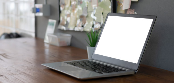 笔记本电脑与白色空白屏幕在木头桌上。工作空间，工作场所，桌面办公的概念。图片下载