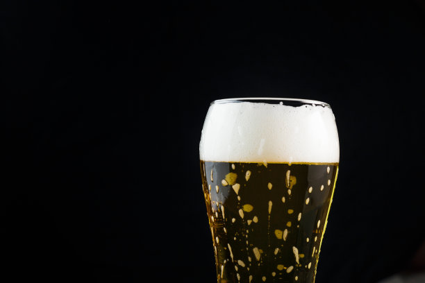 啤酒装在深色背景的玻璃杯里。啤酒泡沫顺着杯壁流下来图片下载