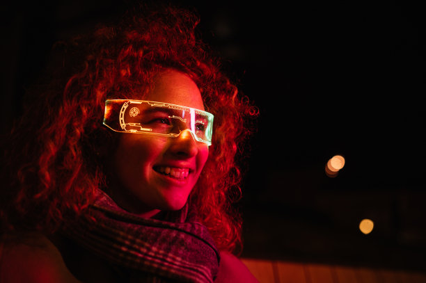 微笑的女人带着发光的智能眼镜在街上。图片下载