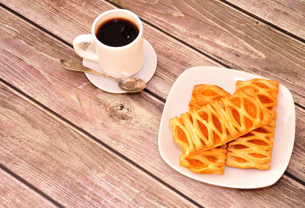 一杯热咖啡放在一个碟子上，有一个勺子，一个盘子里有三个泡芙包和果酱，放在木桌上。图片下载