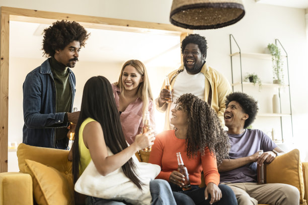 一群年轻的多种族快乐的朋友在公寓里聊天和闲逛。千禧一代的学生在家里喝啤酒。图片下载