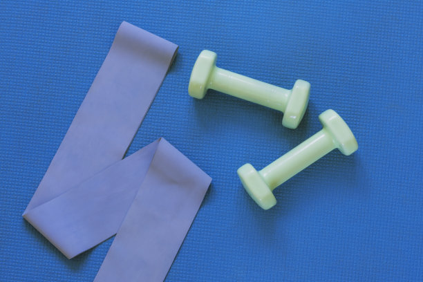 在蓝色运动垫上的哑铃和健身缎带的俯视图。平铺，复制空间。家庭培训概念图片下载