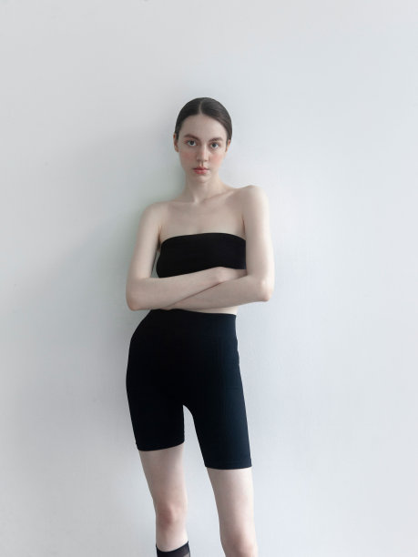 时装模特摆姿势年轻苗条高大美丽的女人穿着时髦的衣服黑色露肩上衣自行车短裤长袜和凉鞋工作室拍摄的肖像在光背景女孩自然化妆美丽腮红图片下载