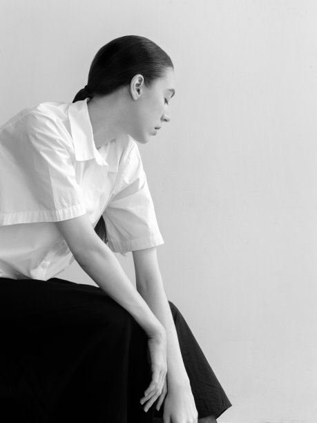 美丽的年轻女子穿着时尚简约的衣服斯堪的纳维亚风格白色短袖衬衫长宽黑色长裙时装模特摆造型看起来富有表现力自信漂亮时装模特工作室肖像在光背景上坐在椅子上图片下载