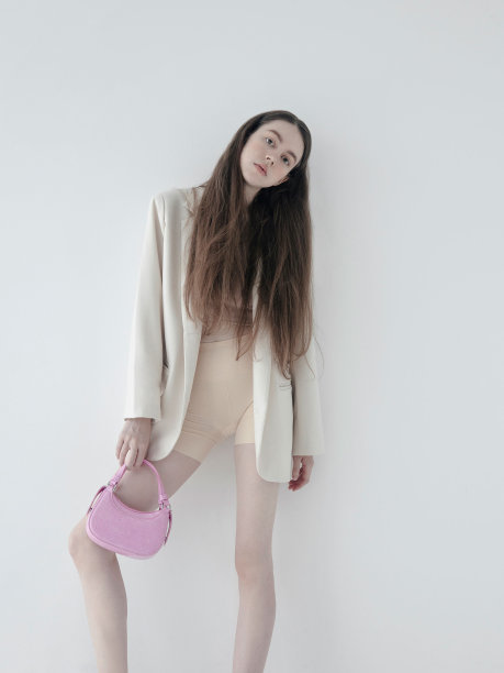 年轻美丽的女孩棕色长发穿着时髦的衣服米色奶油色运动上衣裸色短裤上衣拿着可爱的小粉色包时尚模特工作室肖像在轻背景韩国风格的服装图片下载