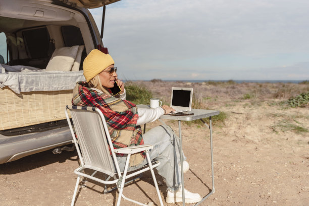 数字游牧妇女在笔记本电脑上工作，用手机聊天，同时带着露营车旅行。现代人生活方式的概念图片下载
