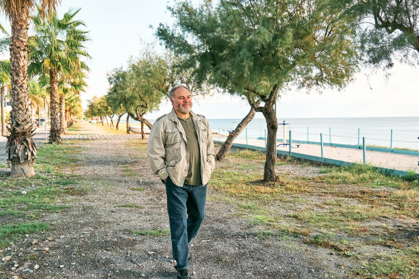 快乐的中年大胡子男子走在海滨长廊。休闲活动、健康、自由、旅游、健康生活方式和自然的概念。图片下载