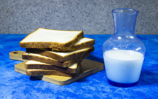 堆叠切片吐司面包在木砧板与瓶牛奶隔离在蓝色垃圾背景图片下载