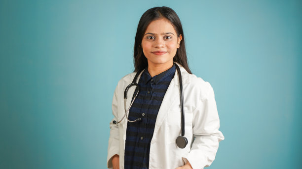一个年轻的女医生穿着围裙和听诊器的肖像，开朗的亚洲印度女医生孤立在蓝色的工作室背景图片下载