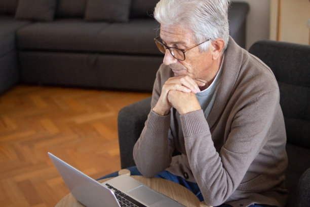 沉思的高级男子看着笔记本电脑屏幕图片下载