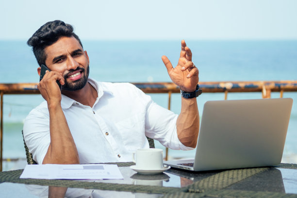 印度暑假男子打电话。时尚年轻的印度男性自由职业者与笔记本电脑自由上网。商人在海滩上远程工作。梦寐以求的工作。网上购销图片下载