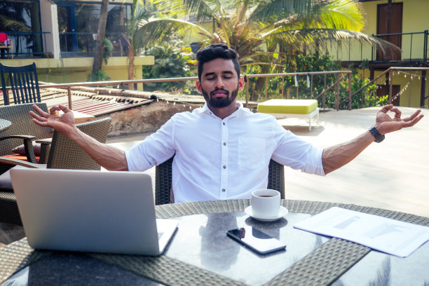 英俊、成功的印度男人，穿着时尚、体面的自由职业者，在海滩上用笔记本电脑工作。一个商人学生在印度洋岸边的夏日咖啡馆里图片下载
